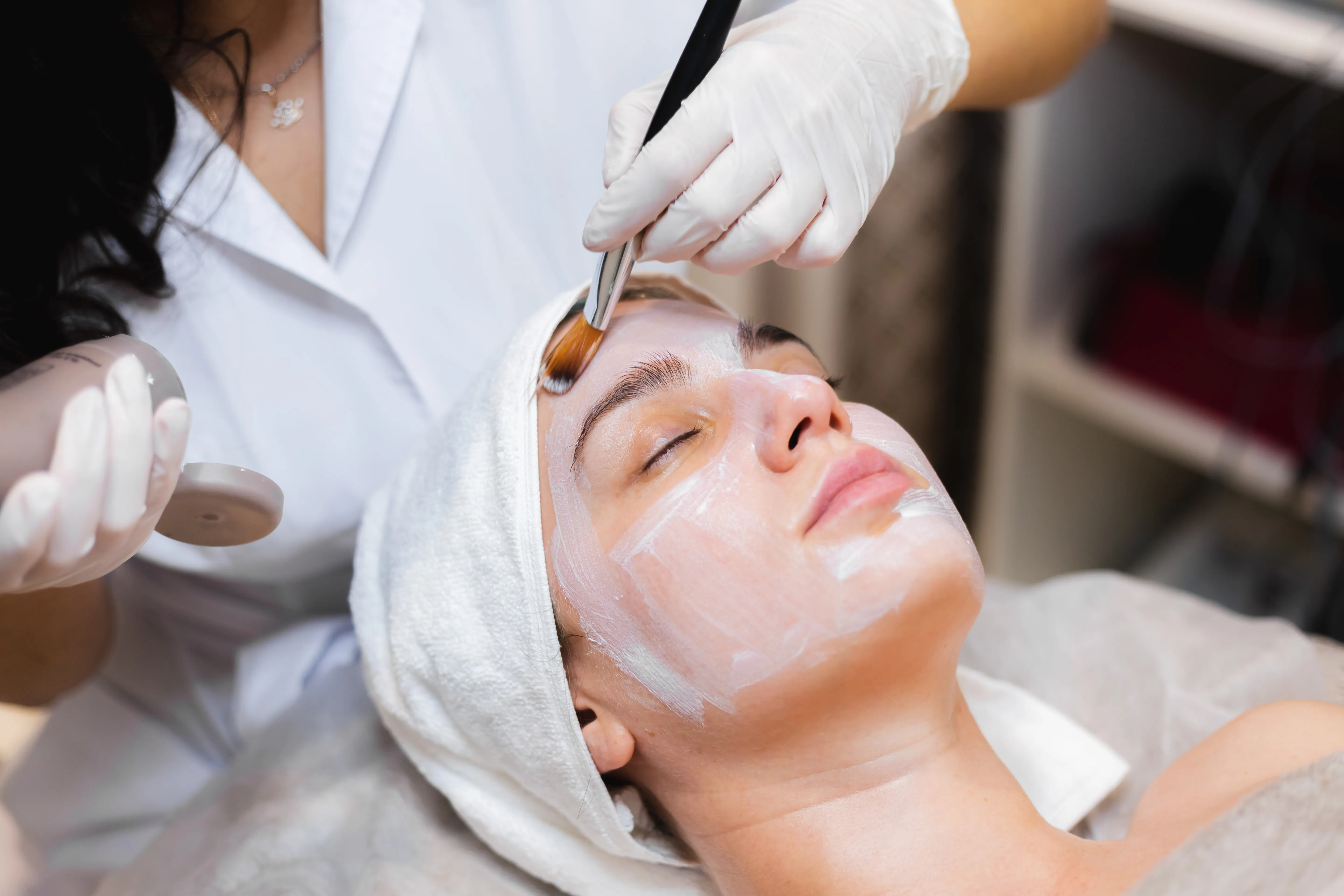A woman undergoing a facial treatment, with soothing products being applied by a skincare specialist in a tranquil spa setting.